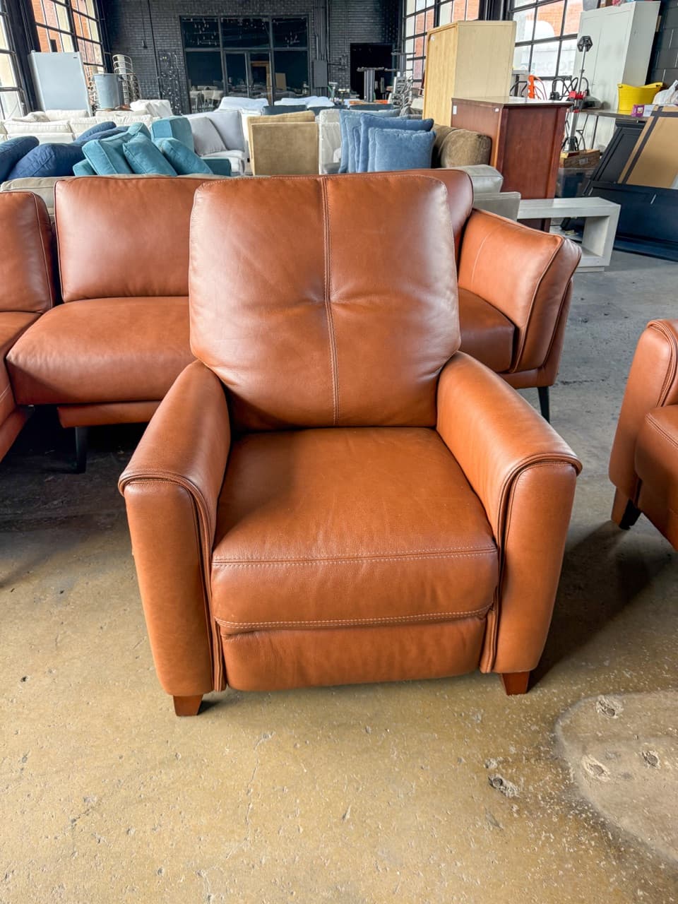 Cognac leather recliner with matching sofa behind it on the warehouse floor
