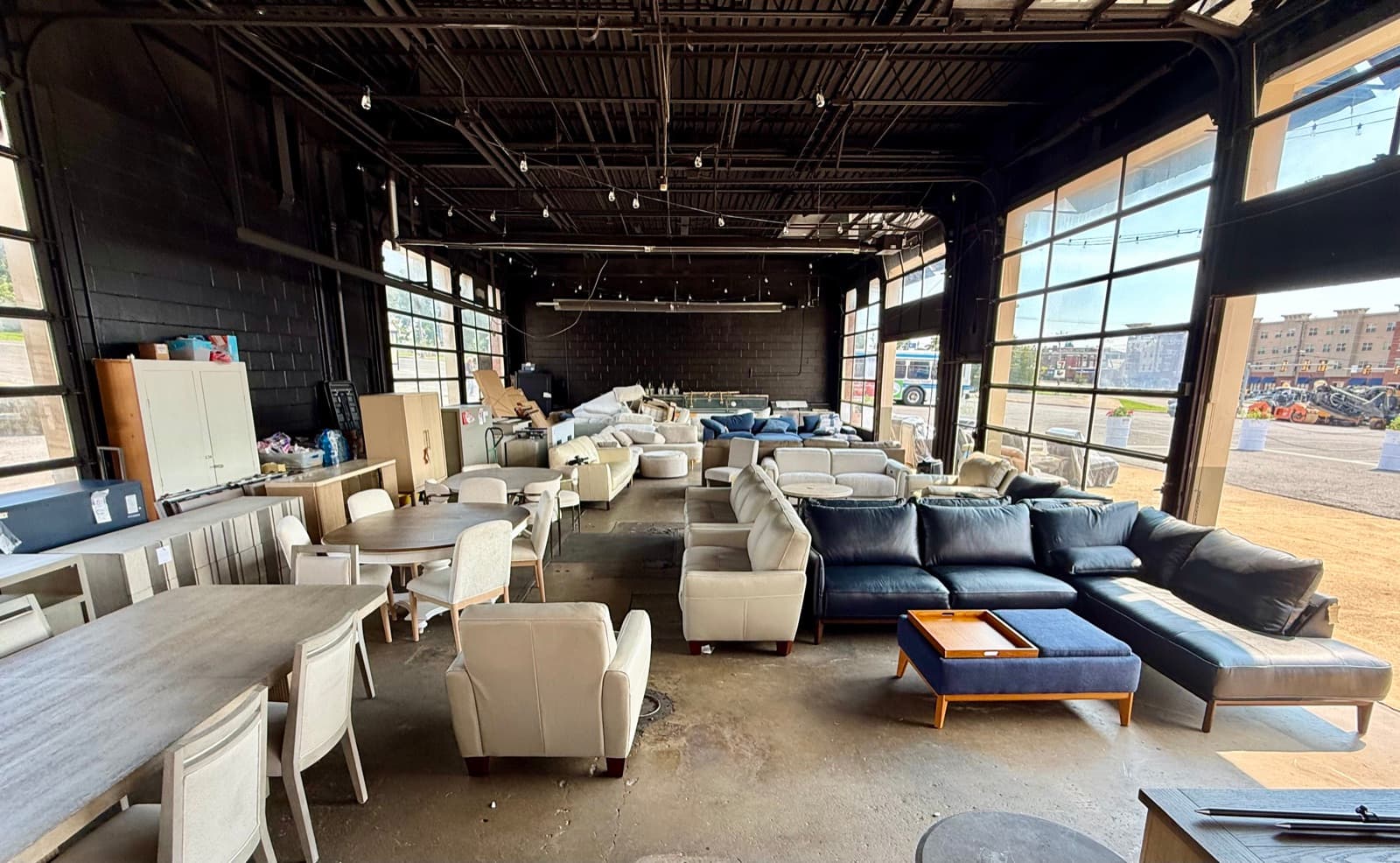 Wide view of the furniture warehouse floor with sectionals, dining sets, and accent chairs near open garage-door windows