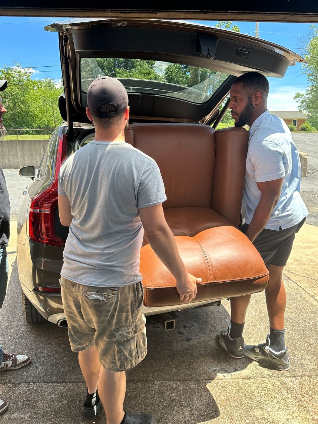 Two men loading a cognac leather armchair into the back of a customer's SUV