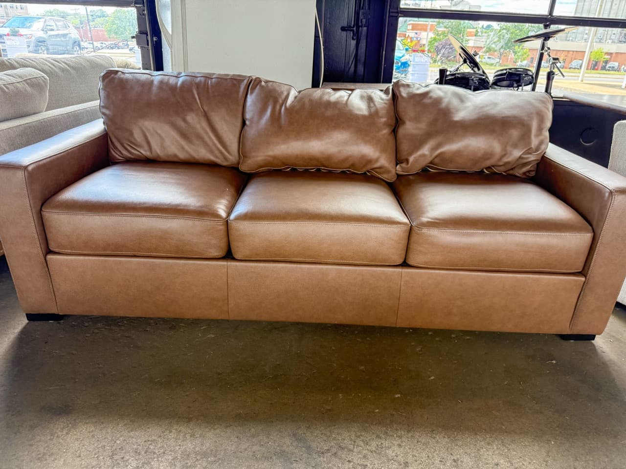 Taupe leather three-seat sofa displayed in front of the showroom windows